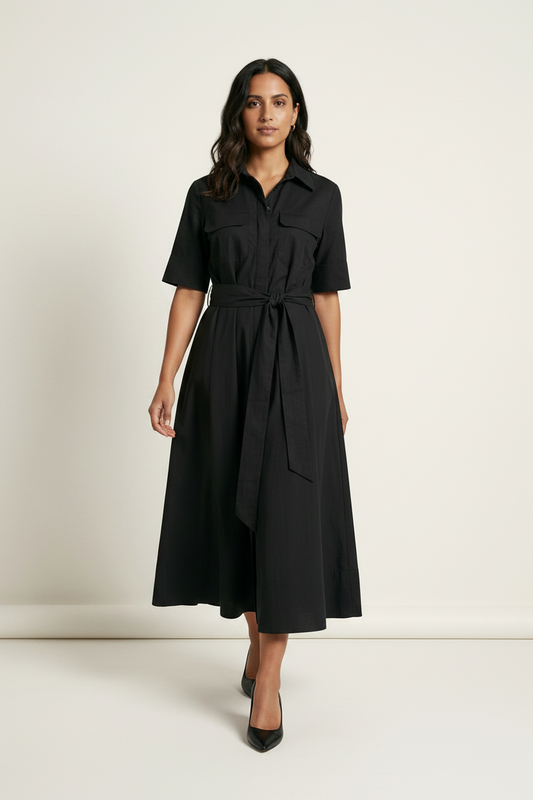 A woman modeling a black short-sleeve midi shirt dress with a tie waist belt, standing against a plain off-white studio background.