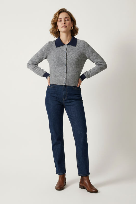 A woman modeling a gray knit zip-front cardigan with contrasting navy blue collar and cuffs, paired with dark blue jeans and brown ankle boots, against a plain light gray studio background.