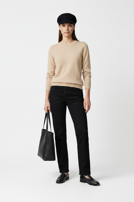 A model stands against a neutral gray studio background wearing a beige knit sweater, black trousers, a black beret, black loafers, and holding a black tote bag.