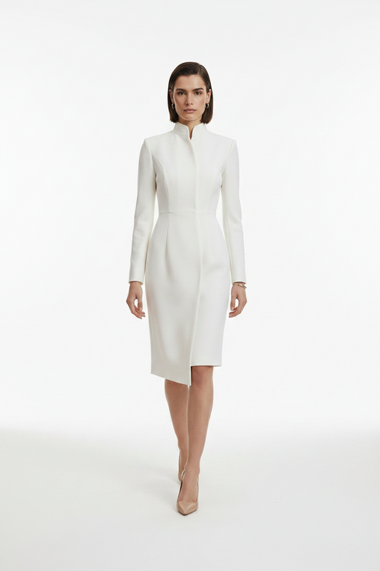 A model wearing a structured white long-sleeve midi dress with a high mock neck and asymmetrical hem, paired with beige pointed-toe heels, against a seamless white studio background.