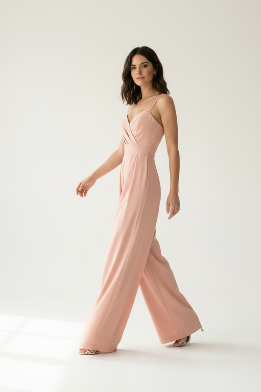 A woman modeling a dusty pink wide-leg jumpsuit with thin spaghetti straps and a sweetheart neckline, standing against a clean white studio background.