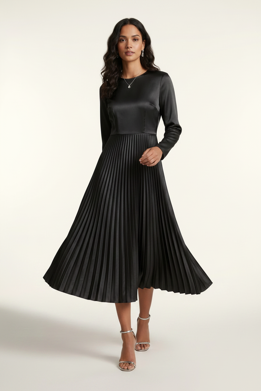 A woman models a black long-sleeve midi dress with a satin-like shiny bodice and a pleated skirt, holding a small silver clutch against a plain light background.
