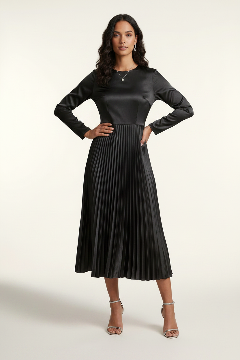 A woman models a black long-sleeve midi dress with a satin-like shiny bodice and a pleated skirt, holding a small silver clutch against a plain light background.