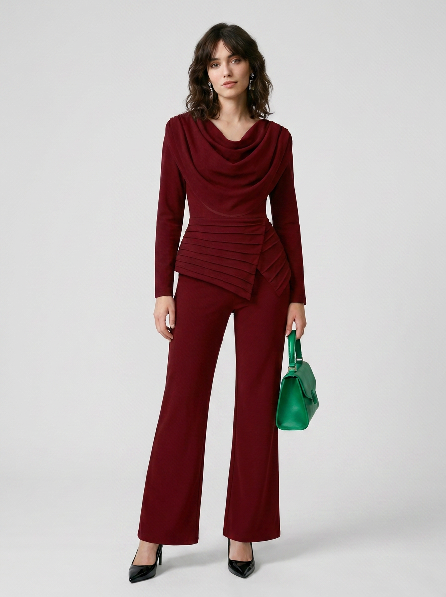 A woman models a matching burgundy two-piece set consisting of a long-sleeve cowl-neck top with a ruched waist and coordinating wide-leg pants, styled with a green handbag and black heels against a light gray studio background.