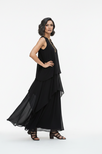 A woman modeling a sleeveless black maxi dress with a layered, flowing skirt against a plain white studio background.