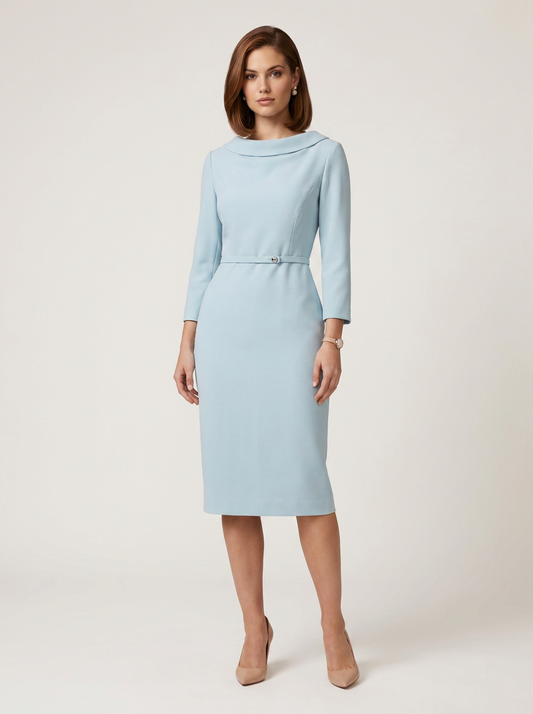 A woman modeling a light blue knee-length dress with three-quarter sleeves, a high draped neckline, and a matching fabric belt with a small metallic center detail, photographed against a plain light beige studio background.