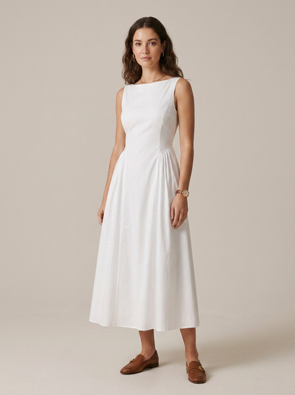 A woman modeling a sleeveless white midi dress with a boat neckline and pleated skirt, paired with brown loafers, against a solid beige studio background.