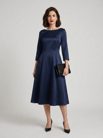 A woman models a navy blue satin midi dress with three-quarter sleeves, a boat neckline, and a flared skirt. She is holding a small black clutch and wearing black pointed-toe heels against a light gray studio background.