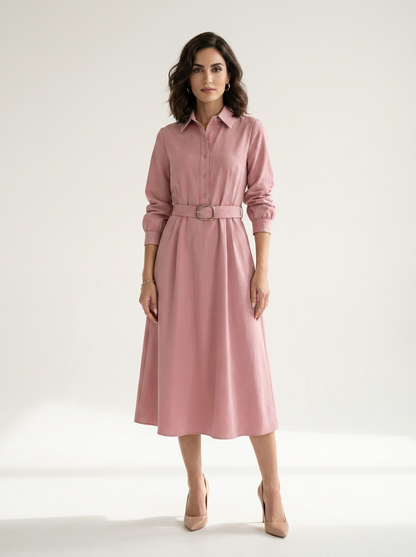 A woman modeling a dusty pink long-sleeve midi shirt dress with a matching belt and silver buckle, styled with beige heels against a plain white studio background.