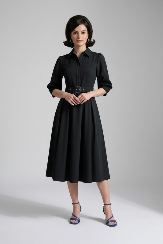 A woman modeling a black midi shirt dress with puff sleeves, a pointed collar, and a matching black belt with a silver buckle, paired with blue strappy heels against a light gray studio background.