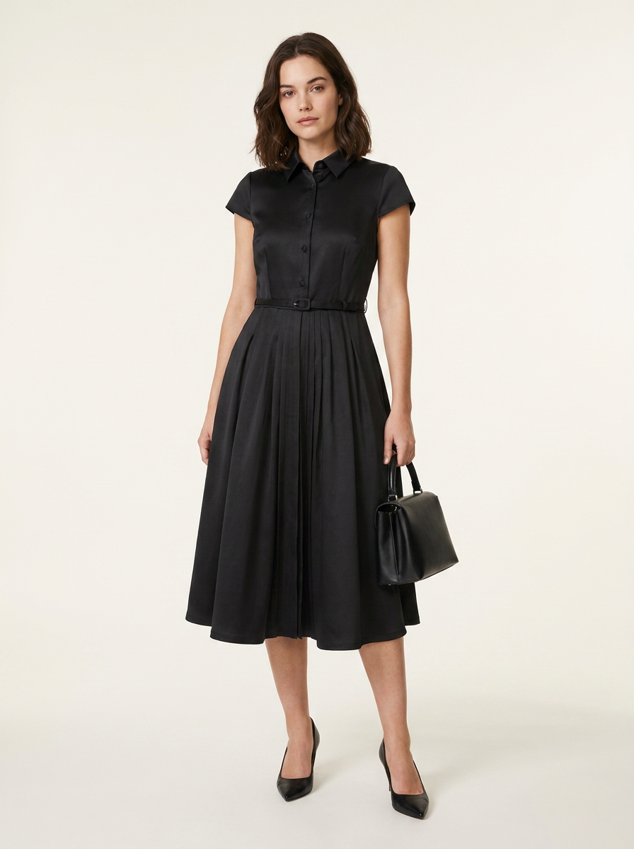 A woman modeling a black short-sleeve midi dress with a button-front bodice and flared skirt, holding a small black handbag against a plain light beige studio background.