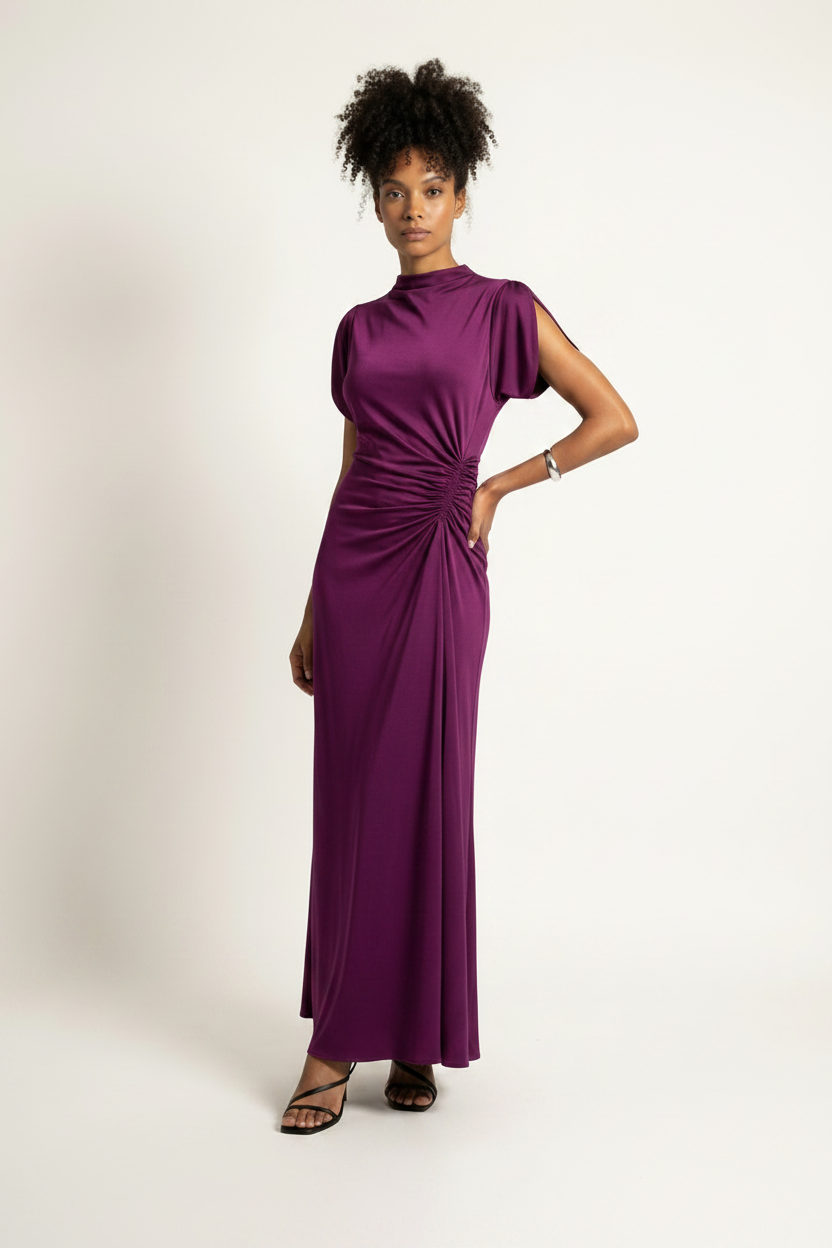 A woman modeling a high-neck, floor-length purple dress with draped short sleeves and gathered detailing at the waist, photographed against a plain light background.
