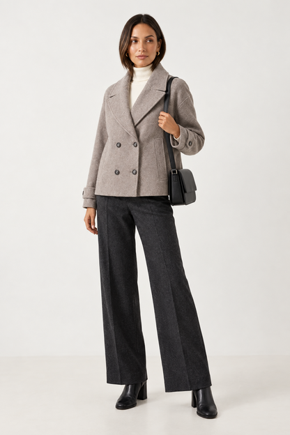 A woman models a light gray double-breasted wool-blend blazer with dark gray wide-leg trousers, a white turtleneck, black ankle boots, and a black shoulder bag against a plain white studio background.