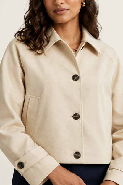 A woman modeling a cropped beige button-front jacket with dark buttons, paired with navy wide-leg trousers and black shoes, against a plain light beige studio background.