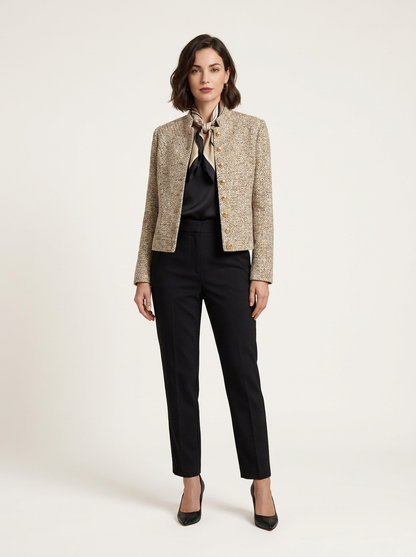 A woman models a cropped beige tweed jacket with gold buttons, worn over a black blouse with a patterned neck scarf and black trousers, against a plain light background.