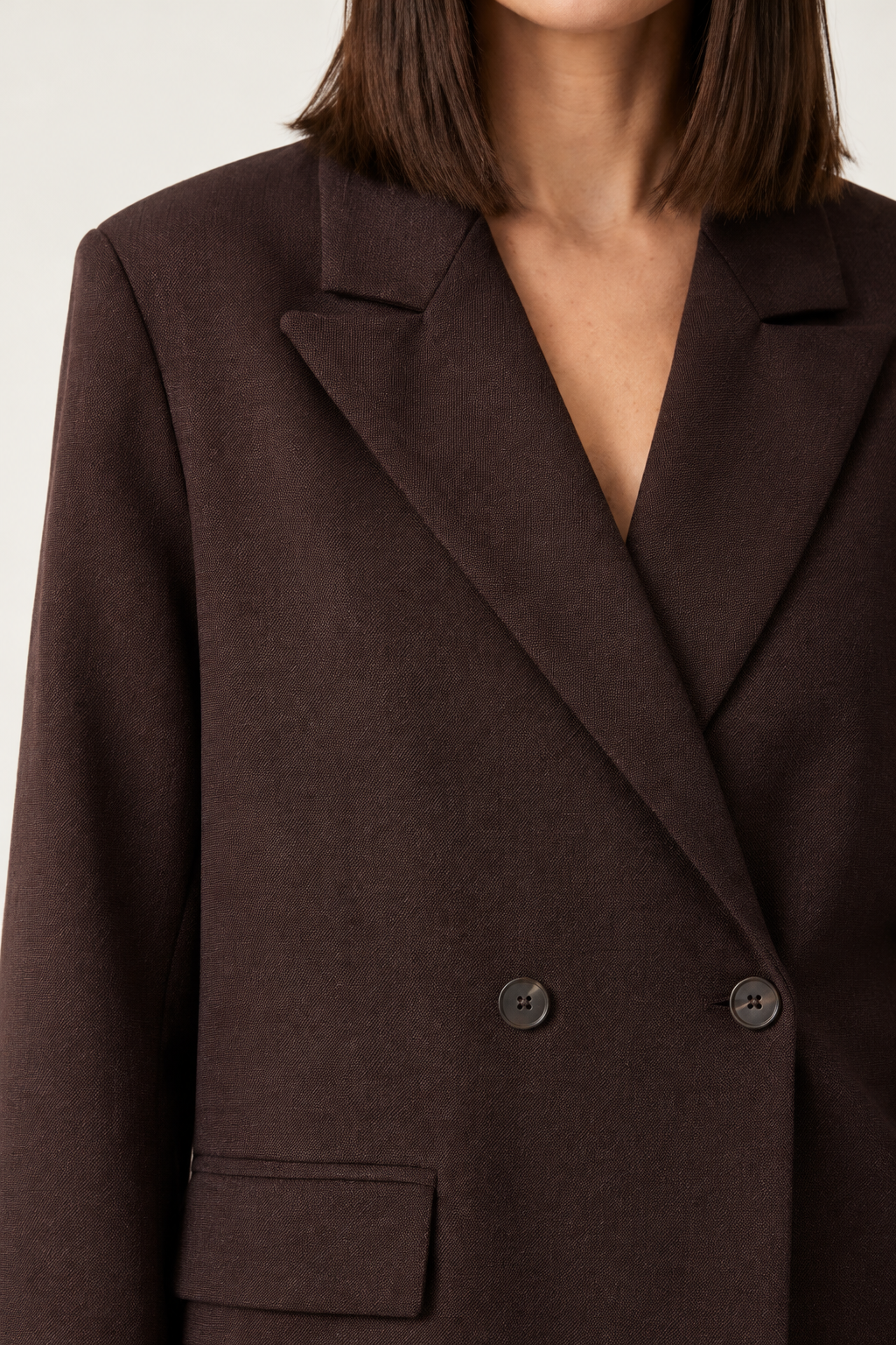 A woman modeling an oversized dark brown double-breasted blazer with light-wash blue jeans, standing against a plain off-white studio background.