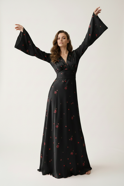 A woman modeling a long black satin-like gown with red floral embroidery, featuring dramatic bell sleeves and a V-neckline, posed with her arms raised against a plain light background.