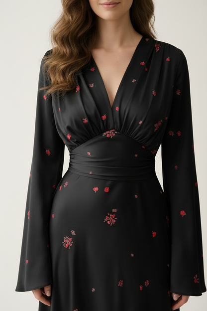 A woman wearing a black long-sleeve wrap-style dress with a gathered waist and scattered small red floral prints, photographed against a plain light background.