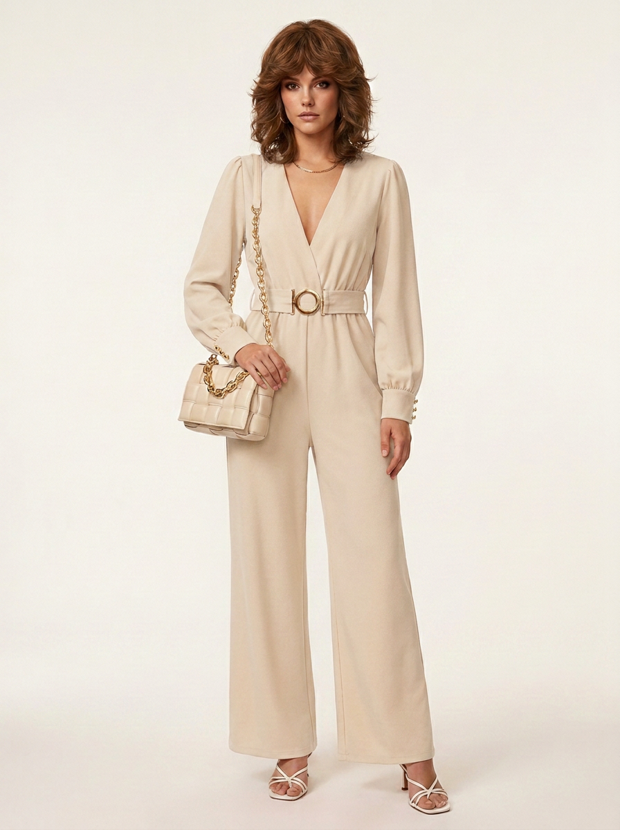 A woman models a beige long-sleeve wide-leg jumpsuit with a matching belt and gold-tone buckle, styled with a matching handbag and strappy heels against a plain light background.