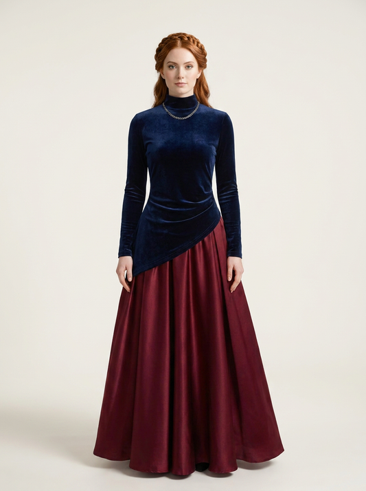 A woman stands against a plain light beige studio background wearing a long-sleeve velvet top with an asymmetrical hem in dark navy blue and a full satin skirt in deep burgundy.
