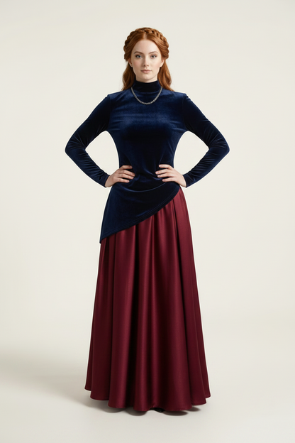 A woman modeling a long-sleeve midi dress with an asymmetrical wrap-style top in deep navy velvet and a flowing satin skirt in burgundy, against a plain light beige studio background.