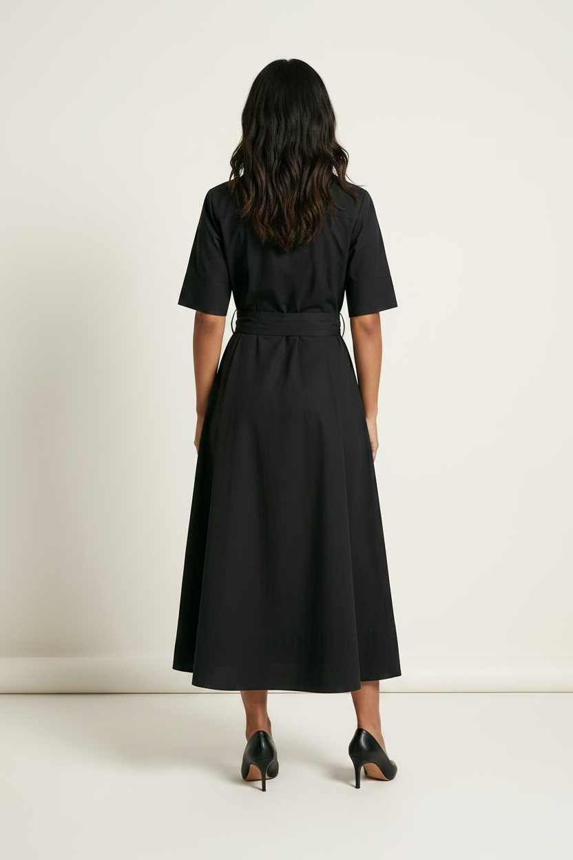 A woman modeling a black short-sleeve midi shirt dress with a tie waist belt, standing against a plain off-white studio background.