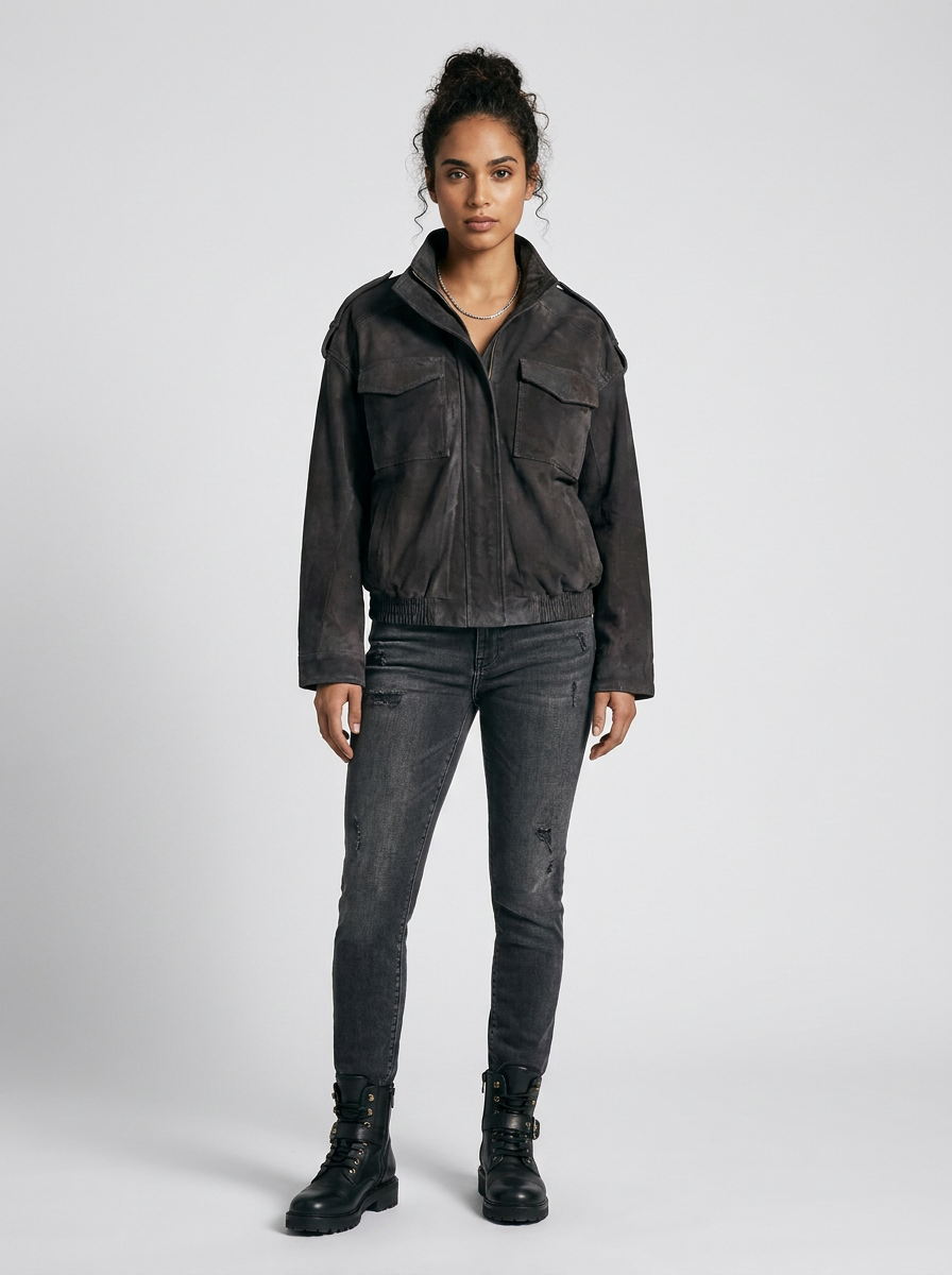 A model stands against a light gray studio background wearing a dark charcoal gray cropped jacket, dark gray distressed skinny jeans, and black combat boots.