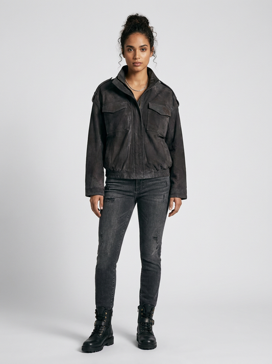 A model stands against a light gray studio background wearing a dark charcoal gray cropped jacket, dark gray distressed skinny jeans, and black combat boots.