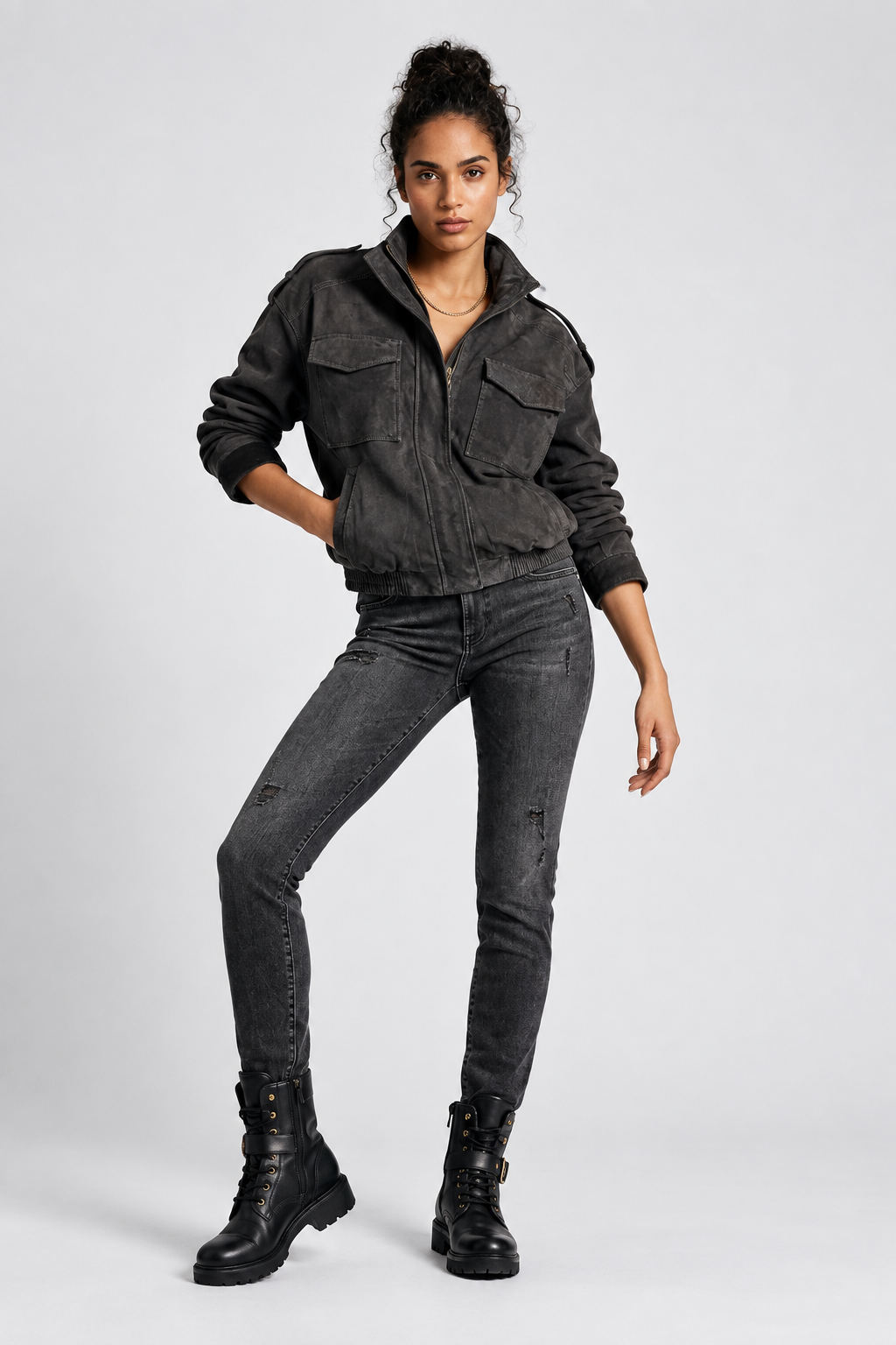 A model posing in a dark washed denim jacket, matching distressed skinny jeans, and black combat boots against a light gray studio background.