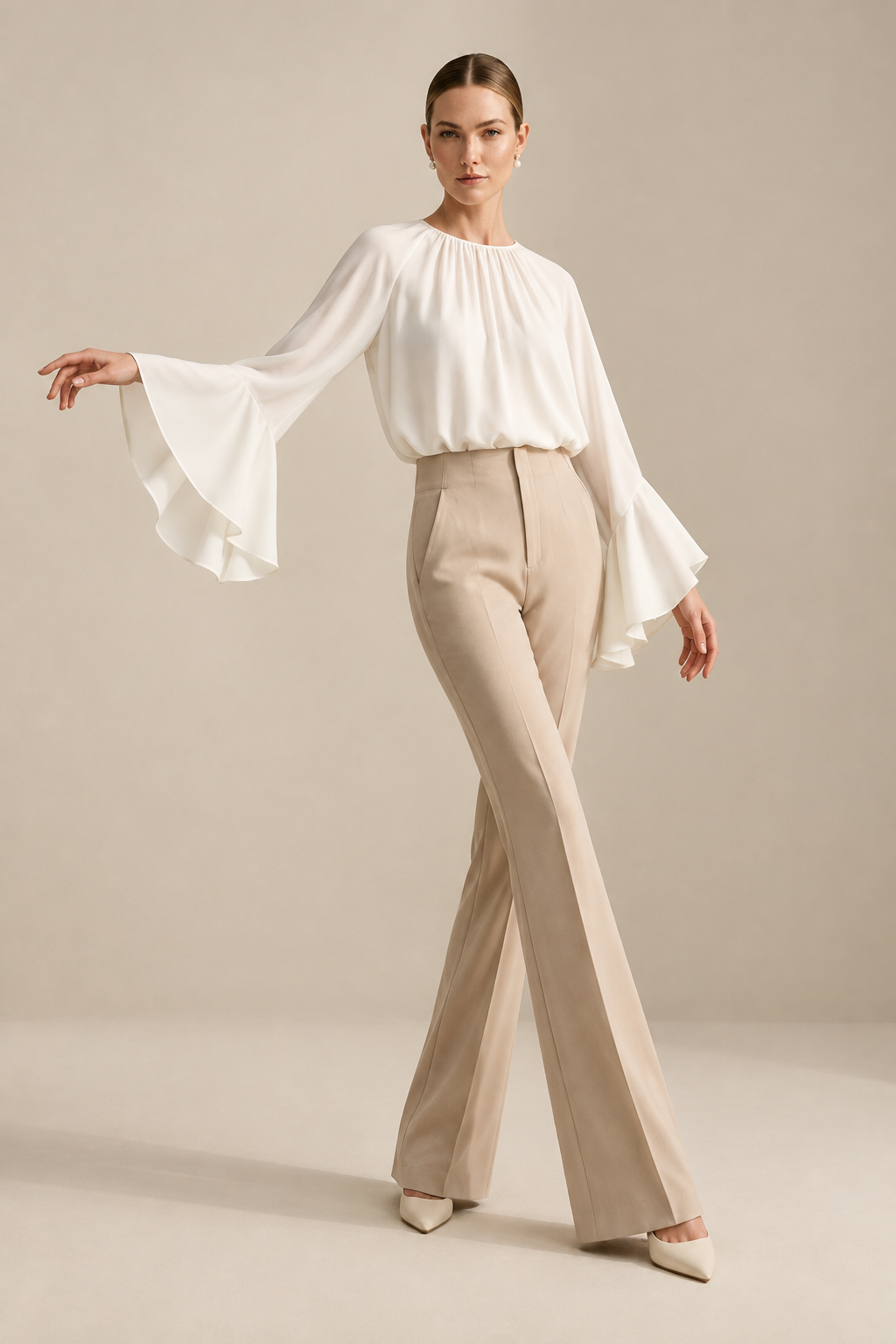 A woman modeling a white long-sleeve blouse with dramatic flared bell sleeves and beige high-waisted trousers, standing against a warm beige studio backdrop.