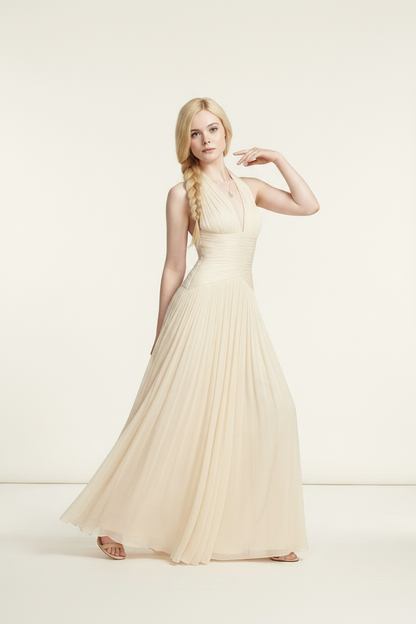 A blonde model wearing a floor-length cream halter gown with a ruched bodice and flowing tulle skirt, standing against a plain cream studio background.