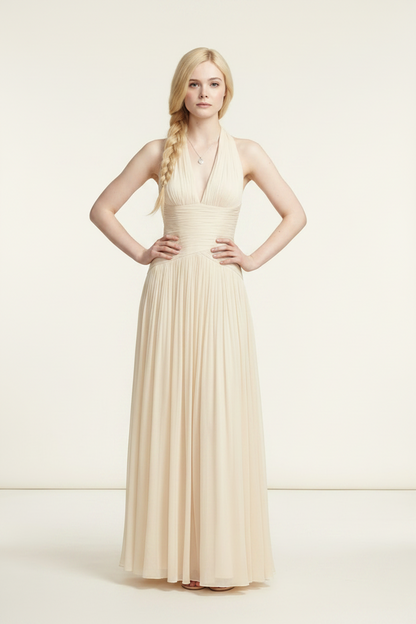 A blonde model wearing a floor-length cream halter gown with a ruched bodice and flowing tulle skirt, standing against a plain cream studio background.