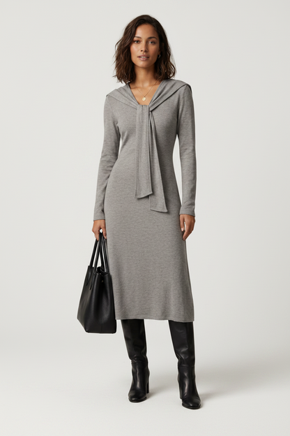 A woman modeling a heather gray long-sleeve midi dress with a wide collar and front tie detail, paired with black knee-high boots and holding a black tote bag against a light gray studio background.