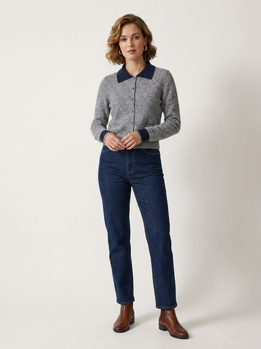 A woman modeling a gray knit zip-front cardigan with contrasting navy blue collar and cuffs, paired with dark blue jeans and brown ankle boots, against a plain light gray studio background.