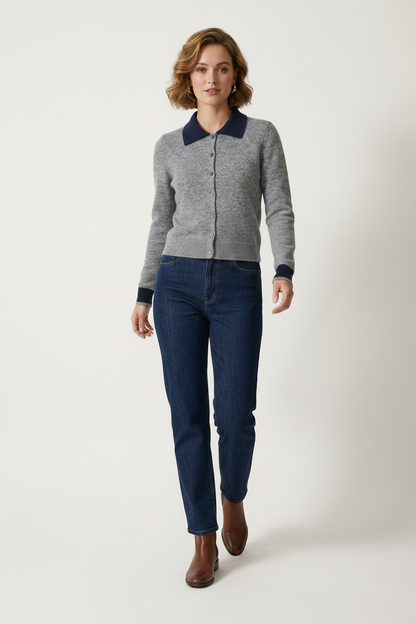 A woman modeling a gray knit zip-front cardigan with contrasting navy blue collar and cuffs, paired with dark blue jeans and brown ankle boots, against a plain light gray studio background.