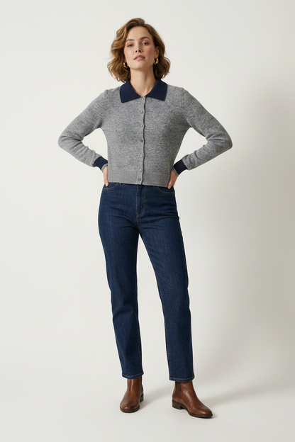A woman modeling a gray knit zip-front cardigan with contrasting navy blue collar and cuffs, paired with dark blue jeans and brown ankle boots, against a plain light gray studio background.