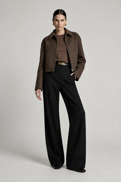 A model stands against a light gray studio background wearing a cropped brown suede jacket over a brown top, black wide-leg trousers, and black shoes.