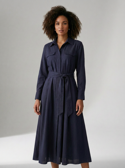 A woman modeling a dark navy blue long-sleeve midi dress with a matching waist tie belt, shown against a neutral light gray studio background.