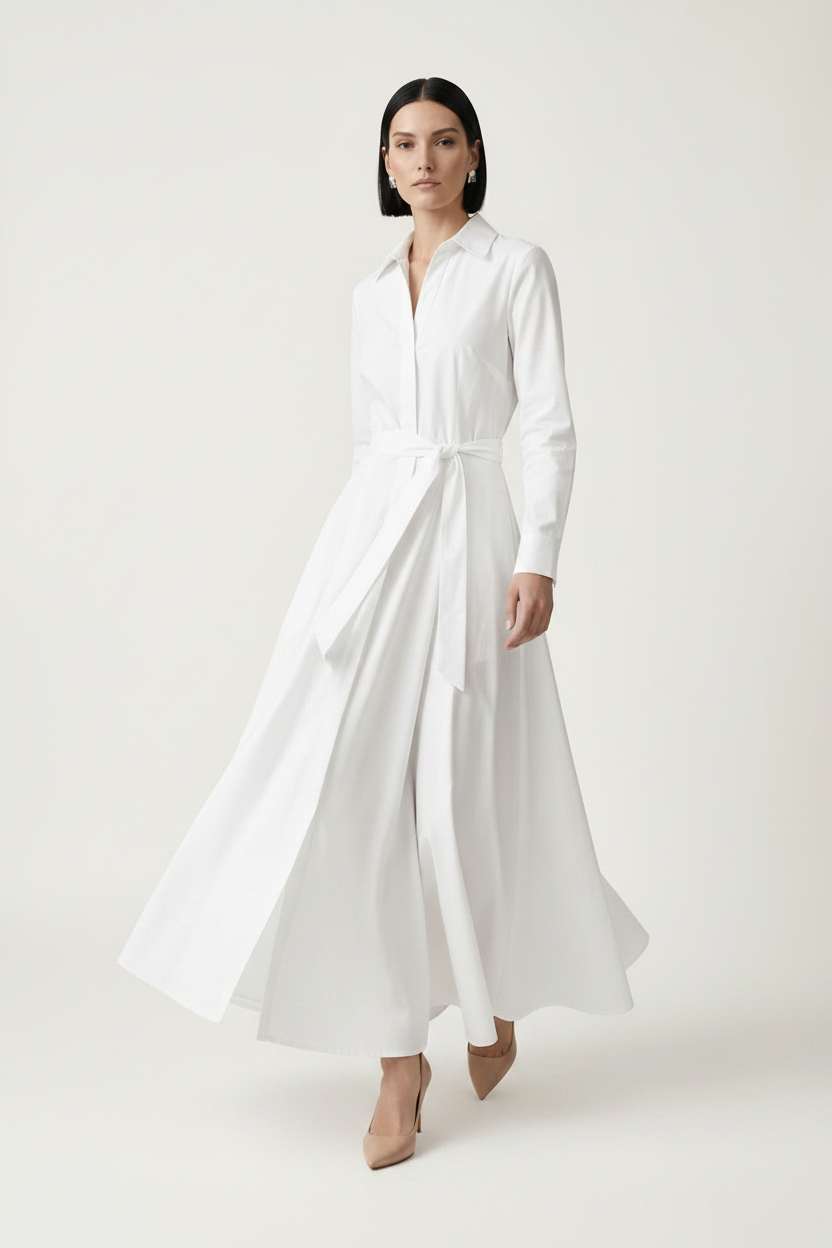 A woman modeling a long-sleeve white shirt dress with a tie waist, standing against a plain light beige studio background.