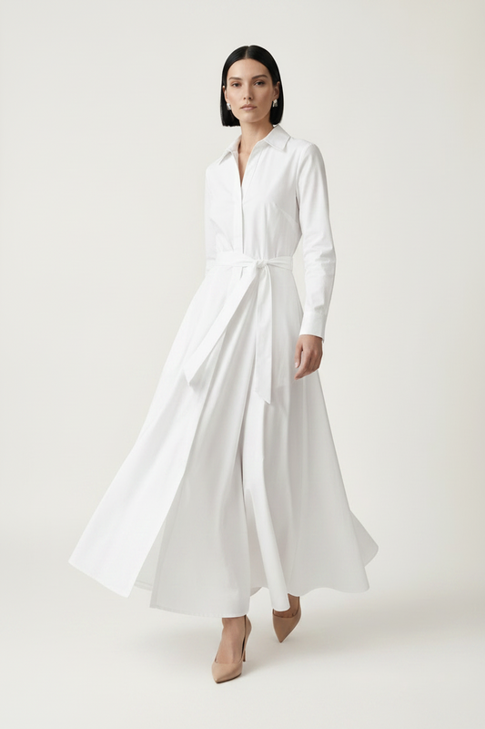 A woman modeling a long-sleeve white shirt dress with a tie waist, standing against a plain light beige studio background.