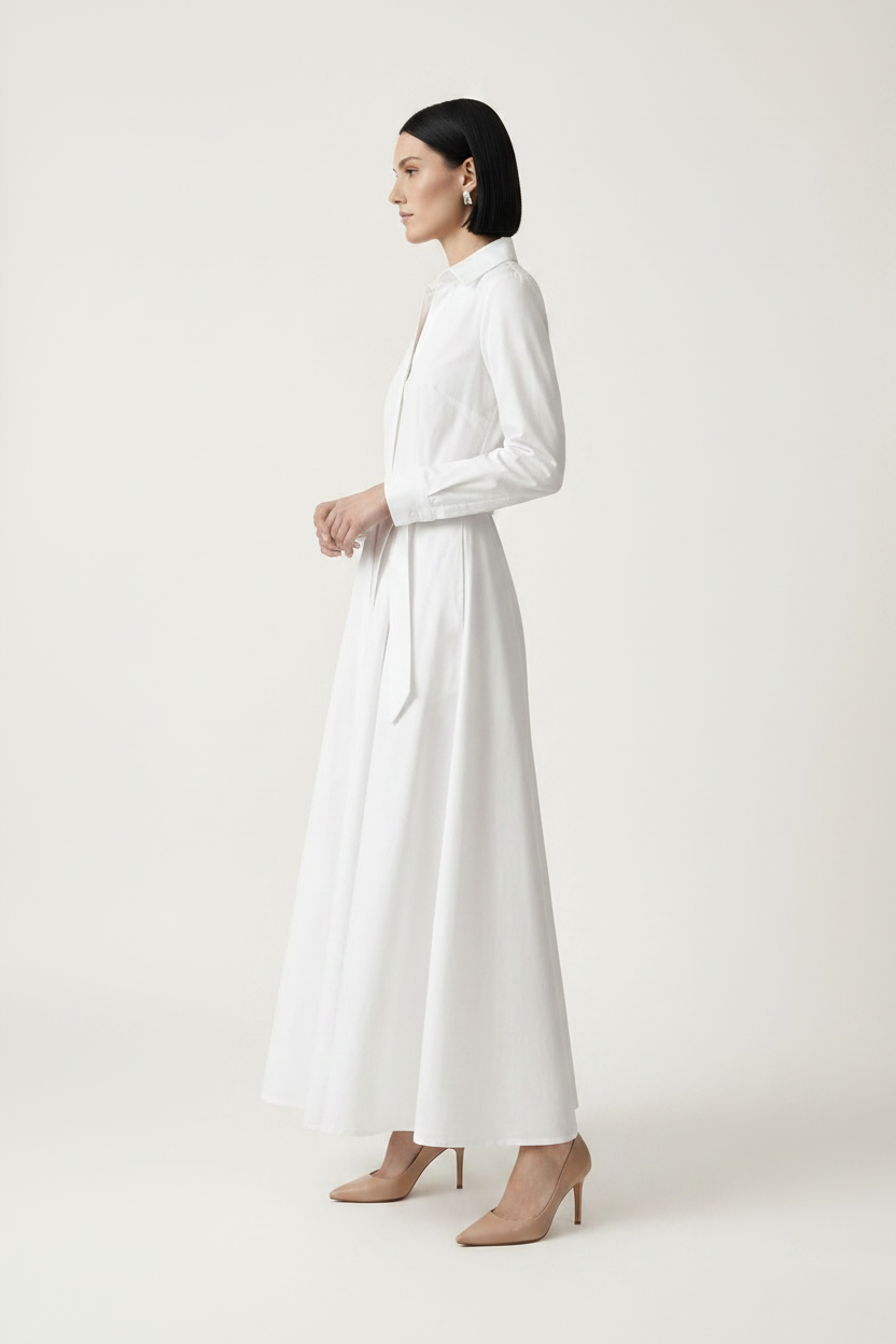 A woman modeling a long-sleeve white shirt dress with a tie waist, standing against a plain light beige studio background.