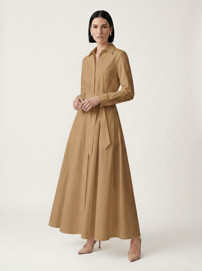 A woman modeling a long-sleeved, collared maxi shirt dress in camel brown against a plain, light beige studio background.
