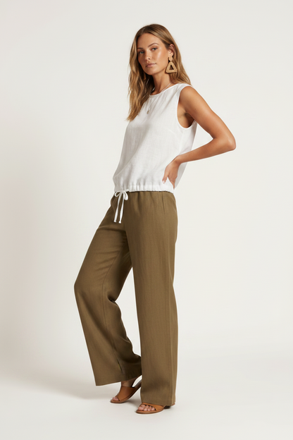 A woman modeling a sleeveless white top and wide-leg olive brown pants against a plain off-white studio background.