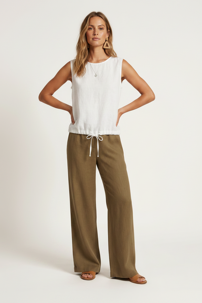 A woman modeling a sleeveless white top and wide-leg olive brown pants against a plain off-white studio background.