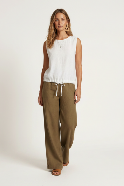 A woman modeling a sleeveless white top and wide-leg olive brown pants against a plain off-white studio background.
