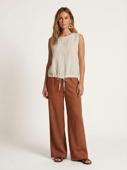 A woman modeling a sleeveless cream top and rust-brown wide-leg pants with a drawstring waist, photographed against a plain light background.