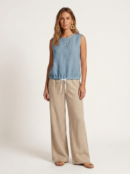 A woman modeling a sleeveless light blue top and beige wide-leg pants with a white drawstring, photographed against a clean off-white studio background.