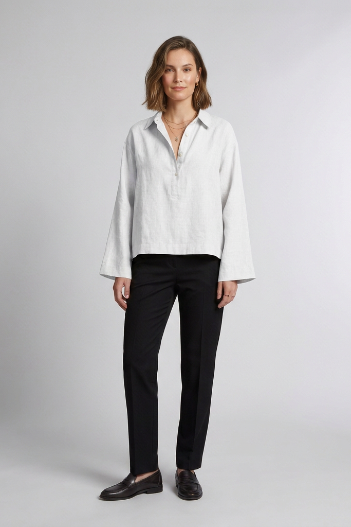 A woman stands against a light gray studio background wearing a Beige long-sleeve button-front blouse with black trousers and dark loafers.