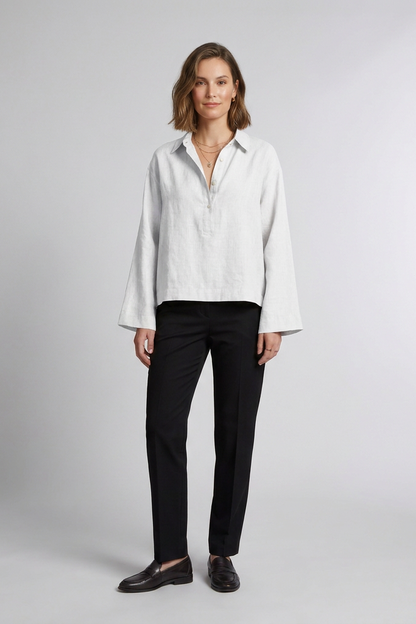 A woman stands against a light gray studio background wearing a Beige long-sleeve button-front blouse with black trousers and dark loafers.
