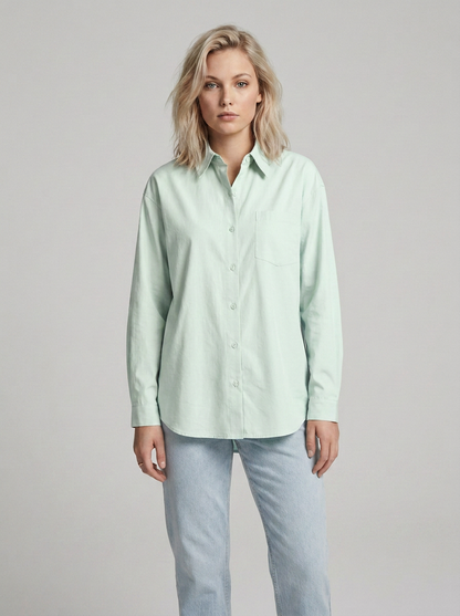 A woman modeling a light mint green long-sleeve button-up shirt with light-wash jeans, standing against a neutral light gray studio background.